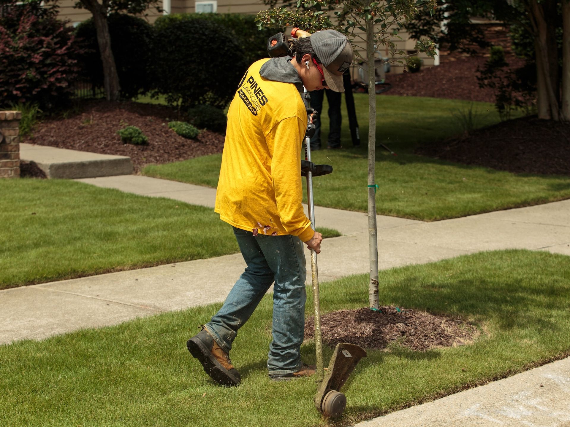 Man in yellow shirt tending to a tree in a grassy yard.