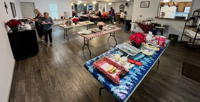 An event room with tables covered in decorative cloths, featuring snacks and centerpieces, with people standing nearby.