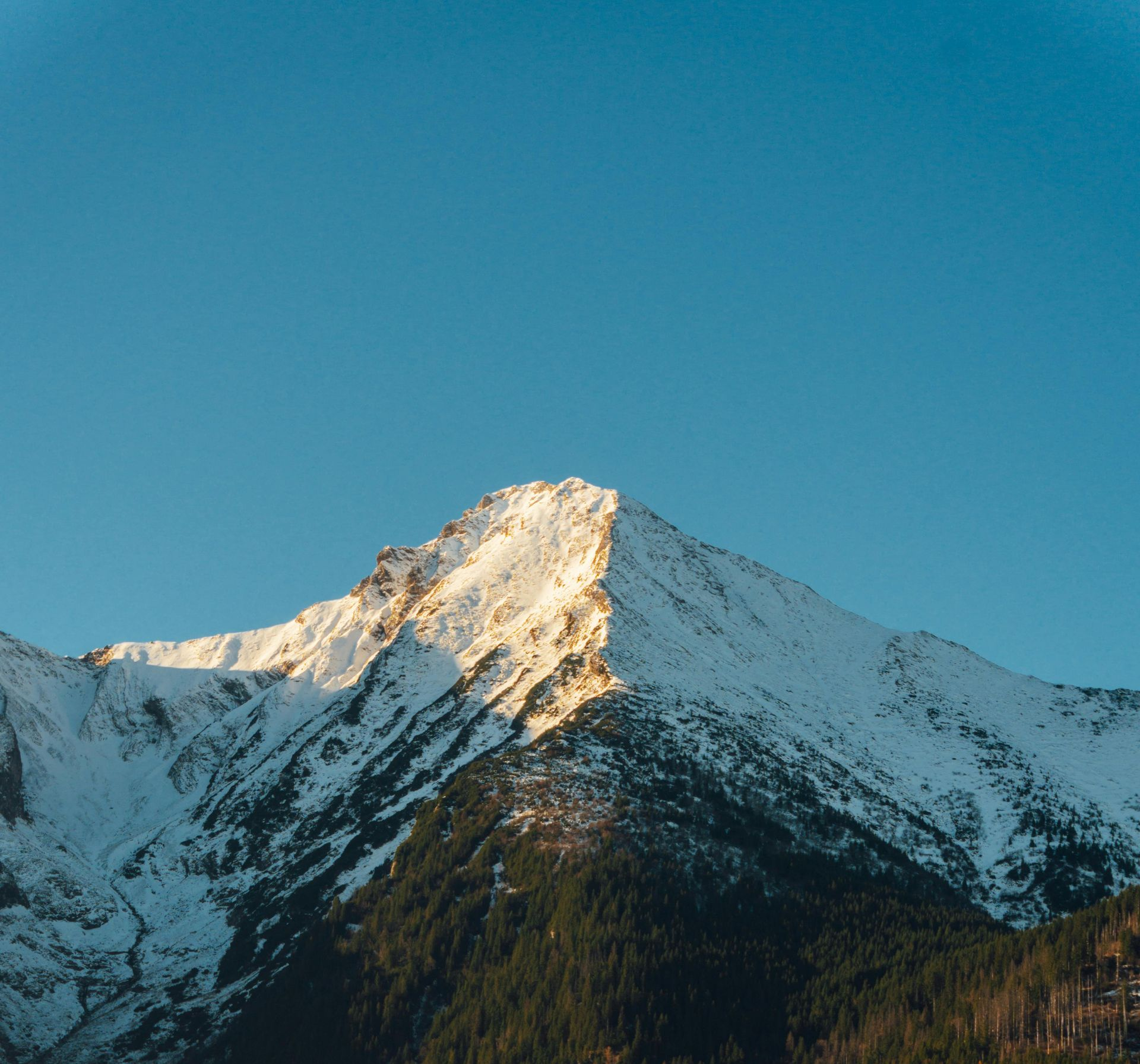 Snow-capped mountain peak lit by sunlight against a clear blue sky.
