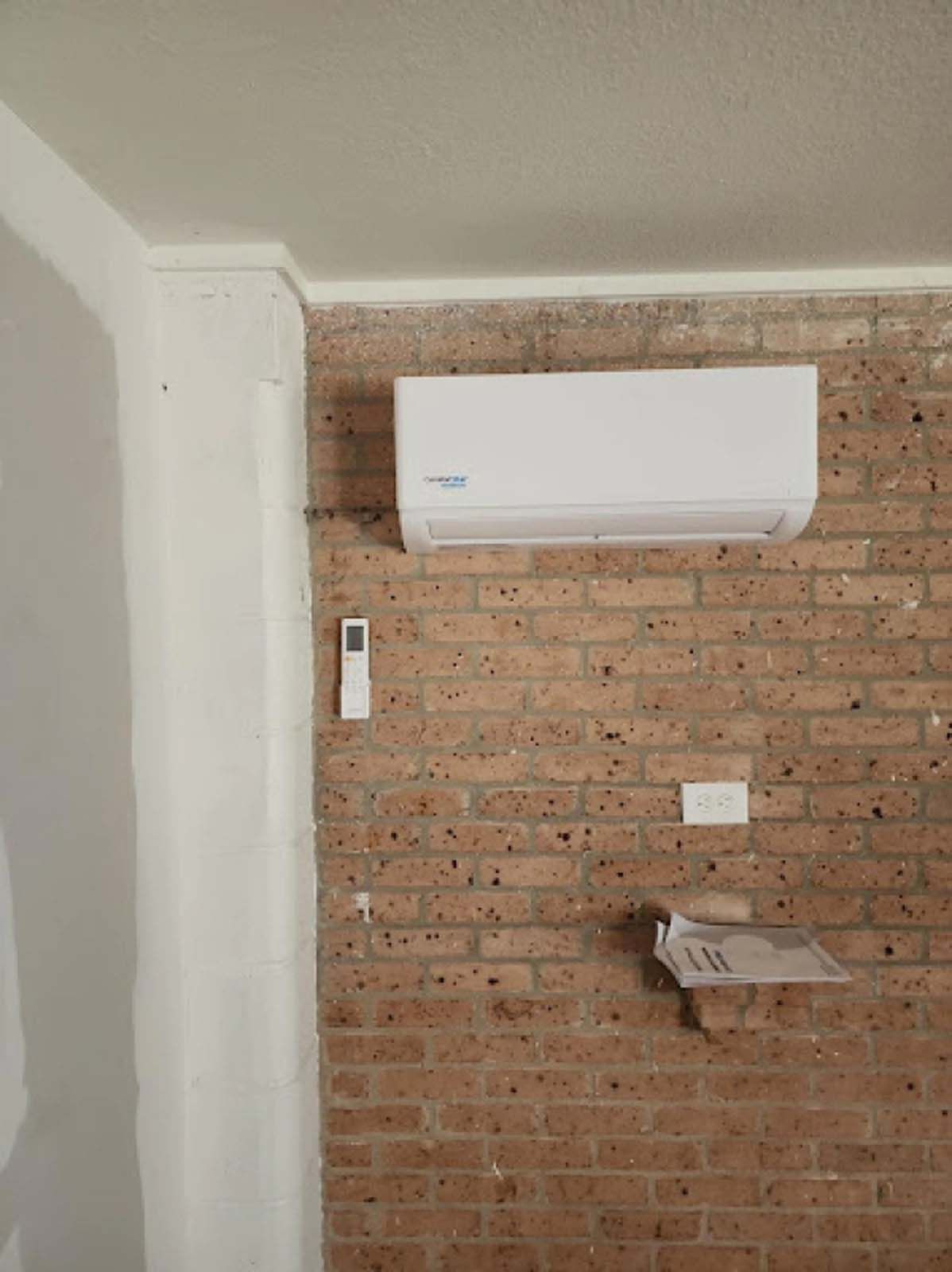 A white air conditioner is mounted on a brick wall in a room.