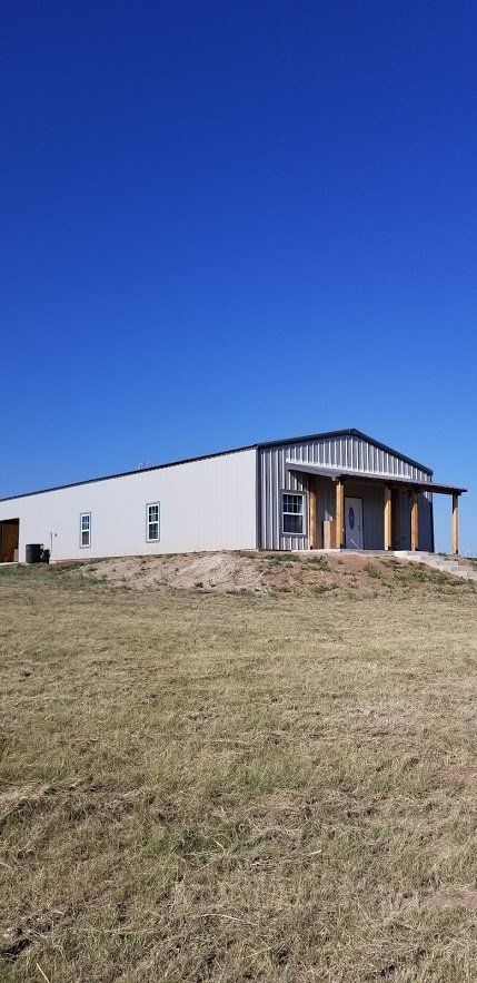 A large white building is sitting in the middle of a grassy field.