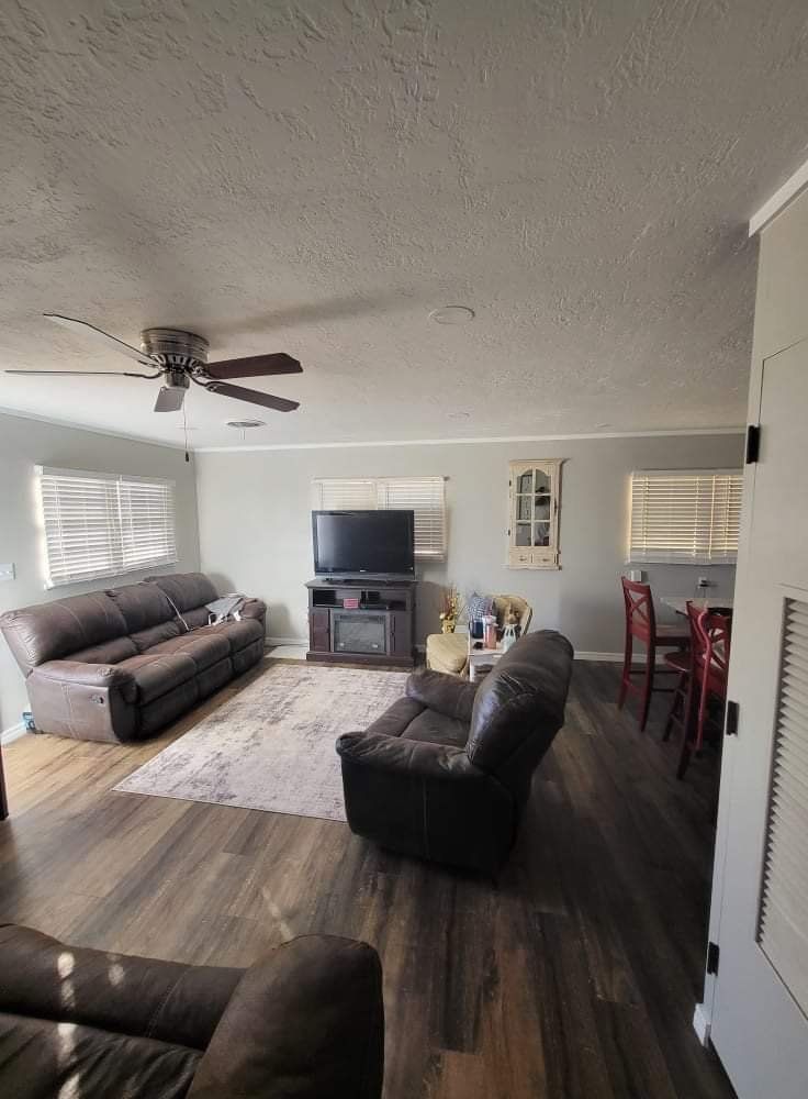 A living room with a couch , chair , television and ceiling fan.