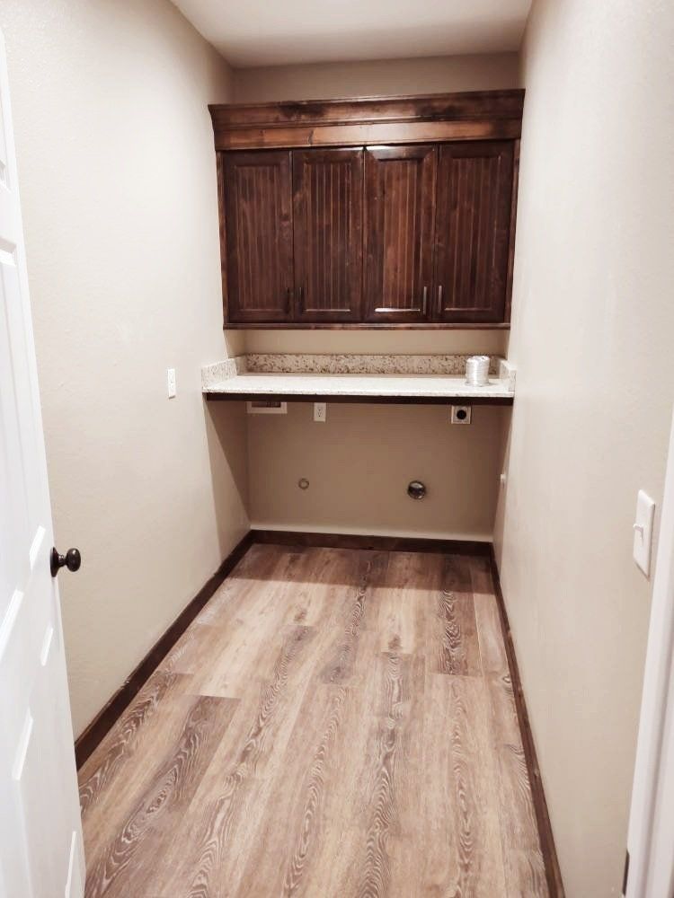 A laundry room with hardwood floors and wooden cabinets