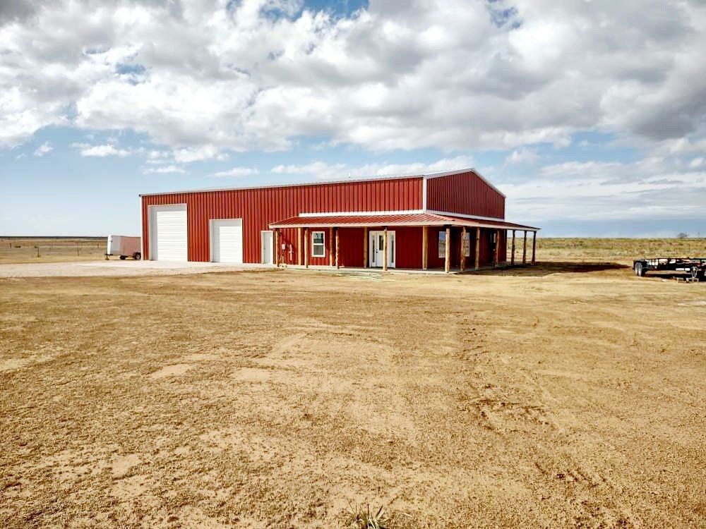 A red barn with a porch is in the middle of a dirt field.