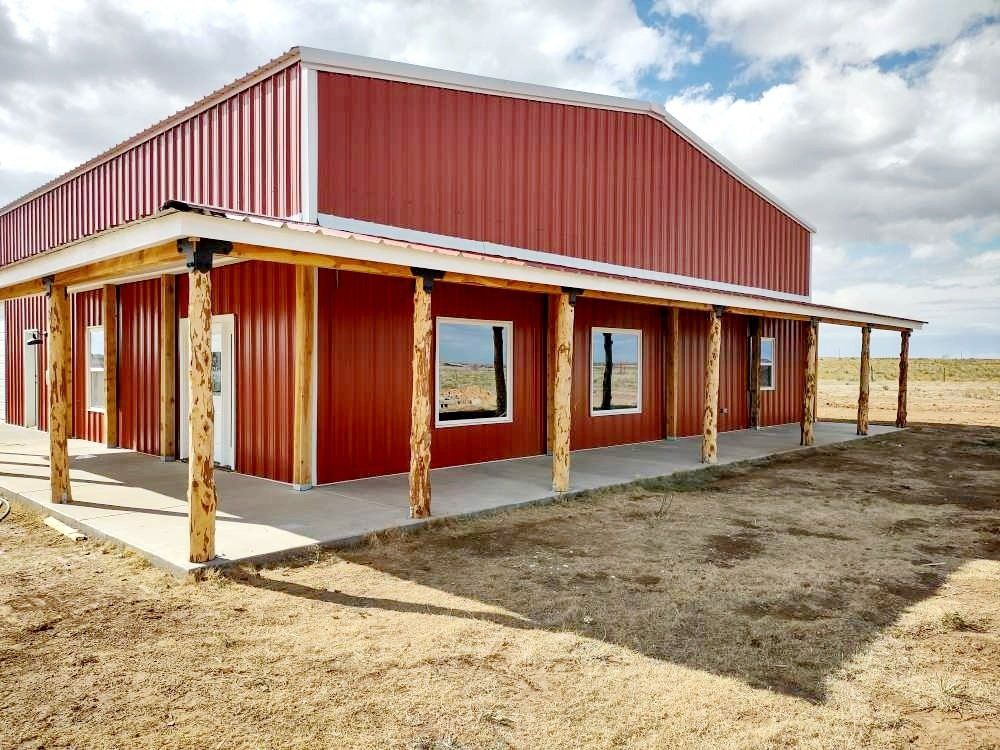 A red barn with a porch and windows in the middle of a field.