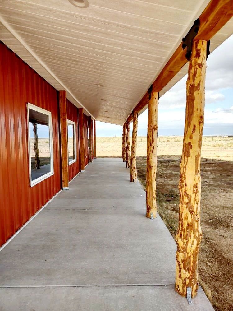 A long concrete porch with wooden posts and a red building in the background