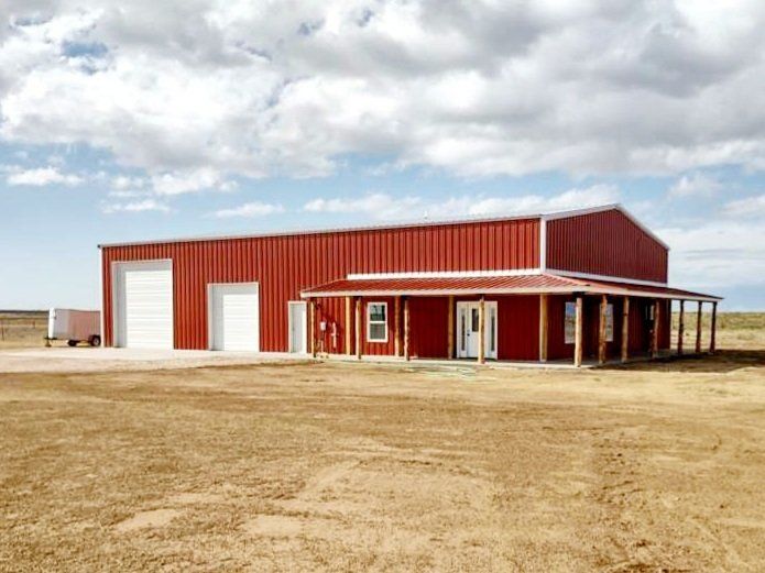 A large red barn with a porch in the middle of a field