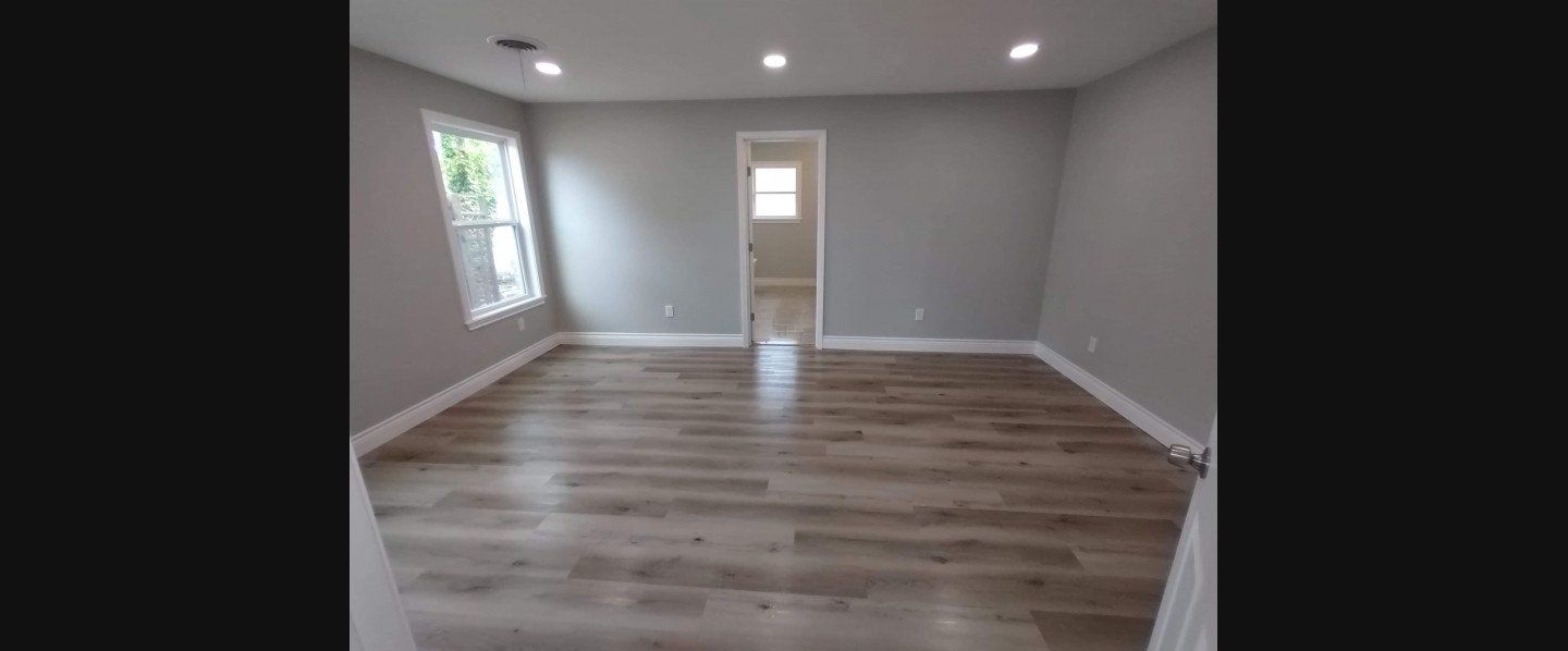An empty living room with hardwood floors and gray walls.