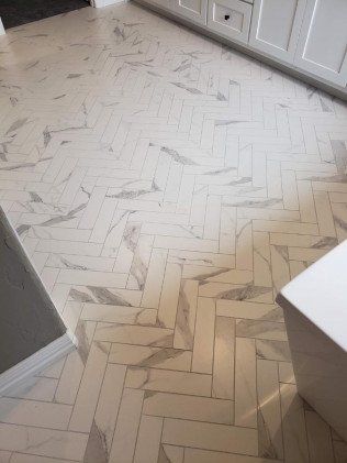 A bathroom with a herringbone tile floor and white cabinets.