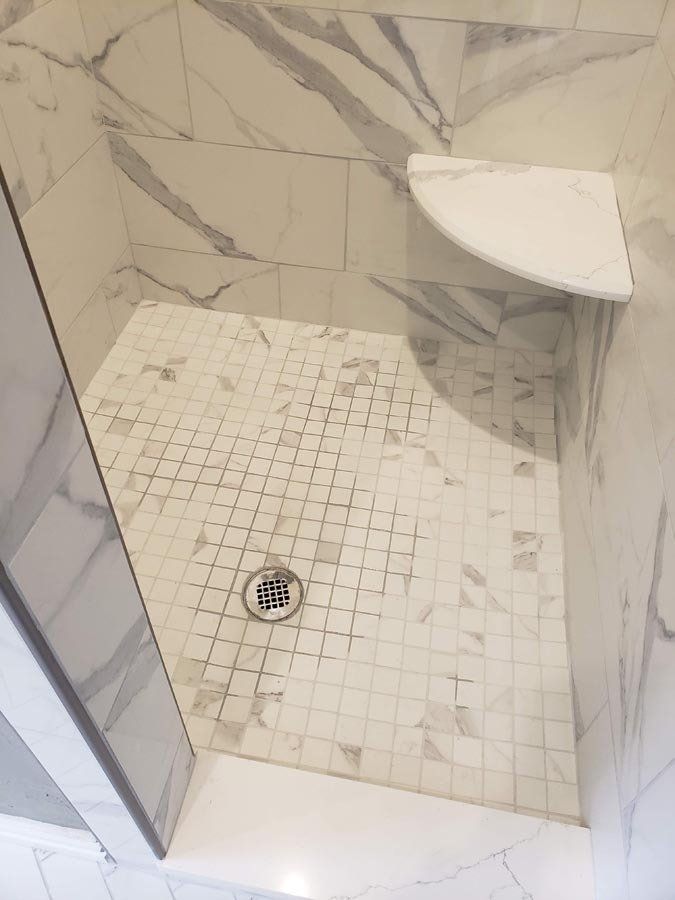 A walk in shower with marble tiles and a drain