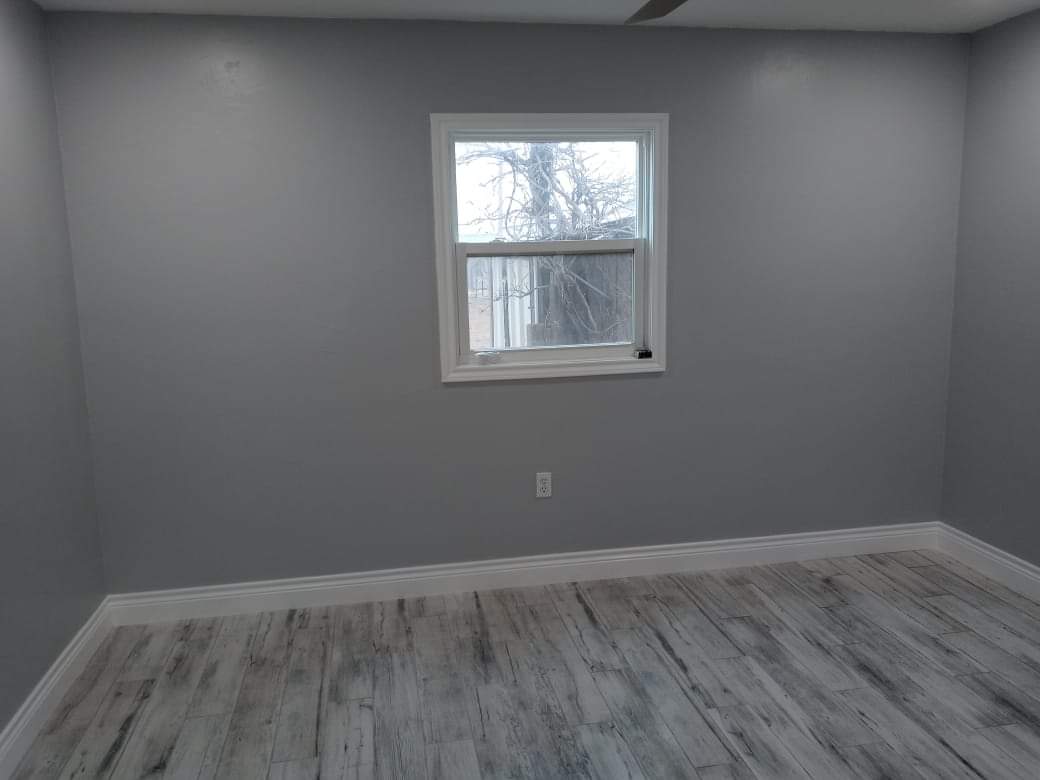 An empty room with a window and a wooden floor.