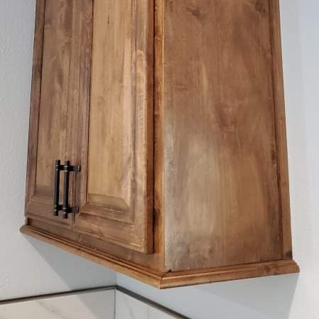 A wooden cabinet with black handles is hanging from the ceiling in a kitchen.