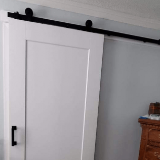 A white sliding barn door with a black railing in a bedroom.