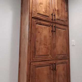 A large wooden cabinet is sitting in a bathroom next to a white wall.