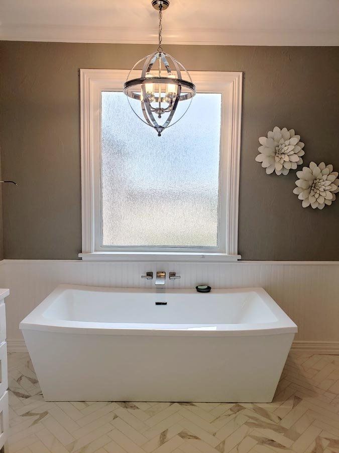 A bathroom with a bathtub and a window with a chandelier hanging from the ceiling.