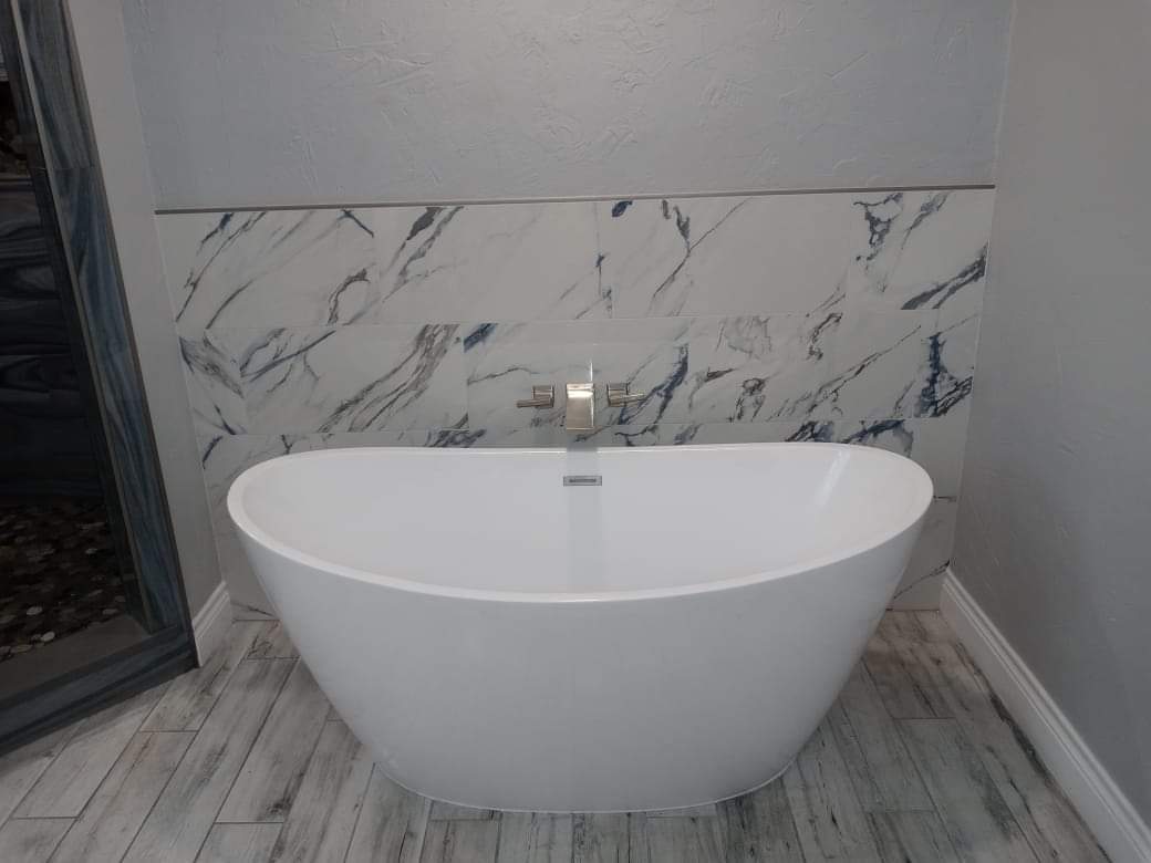 A white bathtub is sitting in a bathroom next to a marble wall.