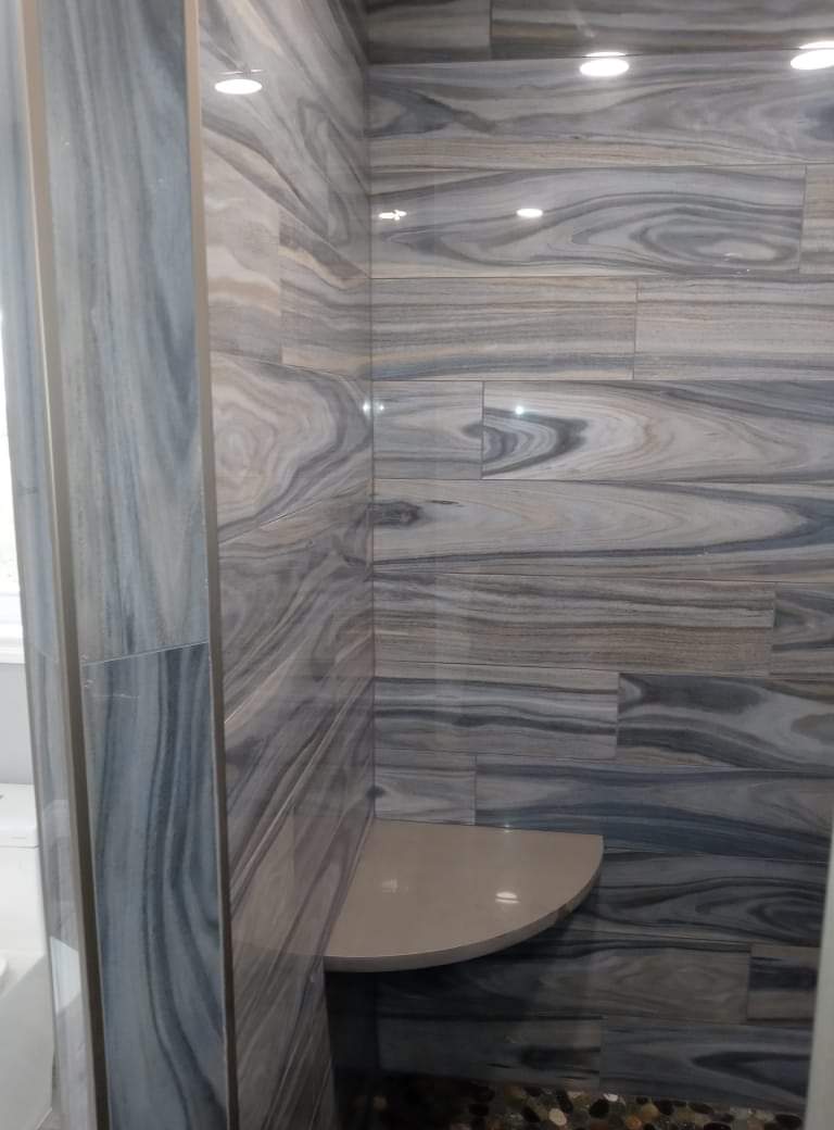 A bathroom with marble tiles on the walls and a bench in the shower.