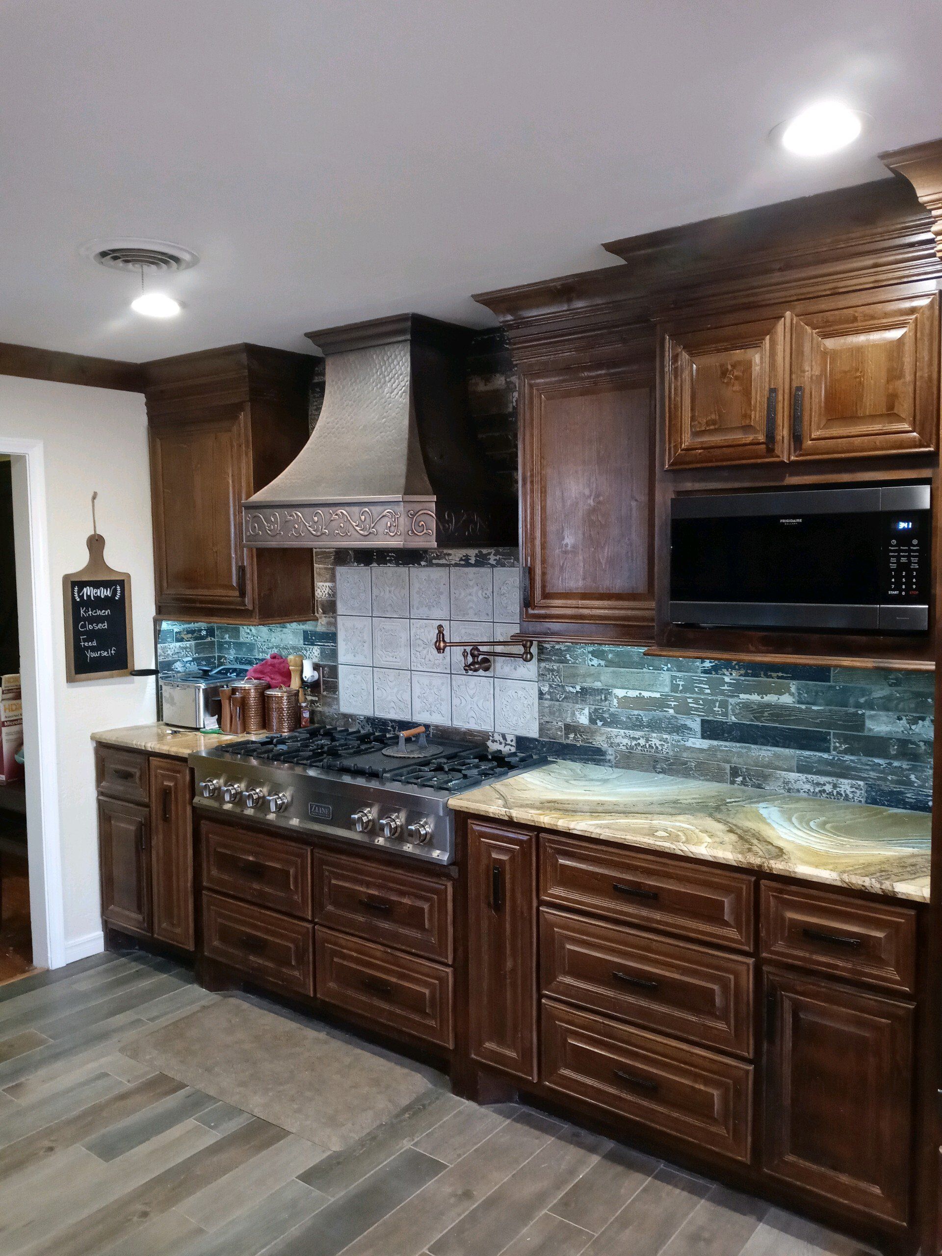 A kitchen with wooden cabinets , a stove , a microwave , and a hood.