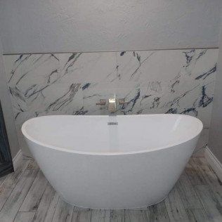 A white bathtub is sitting in a bathroom next to a marble wall.