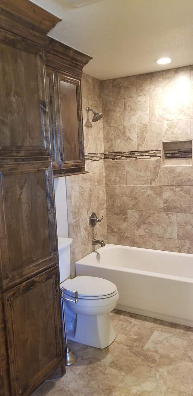 A bathroom with a toilet , tub , shower and cabinets.