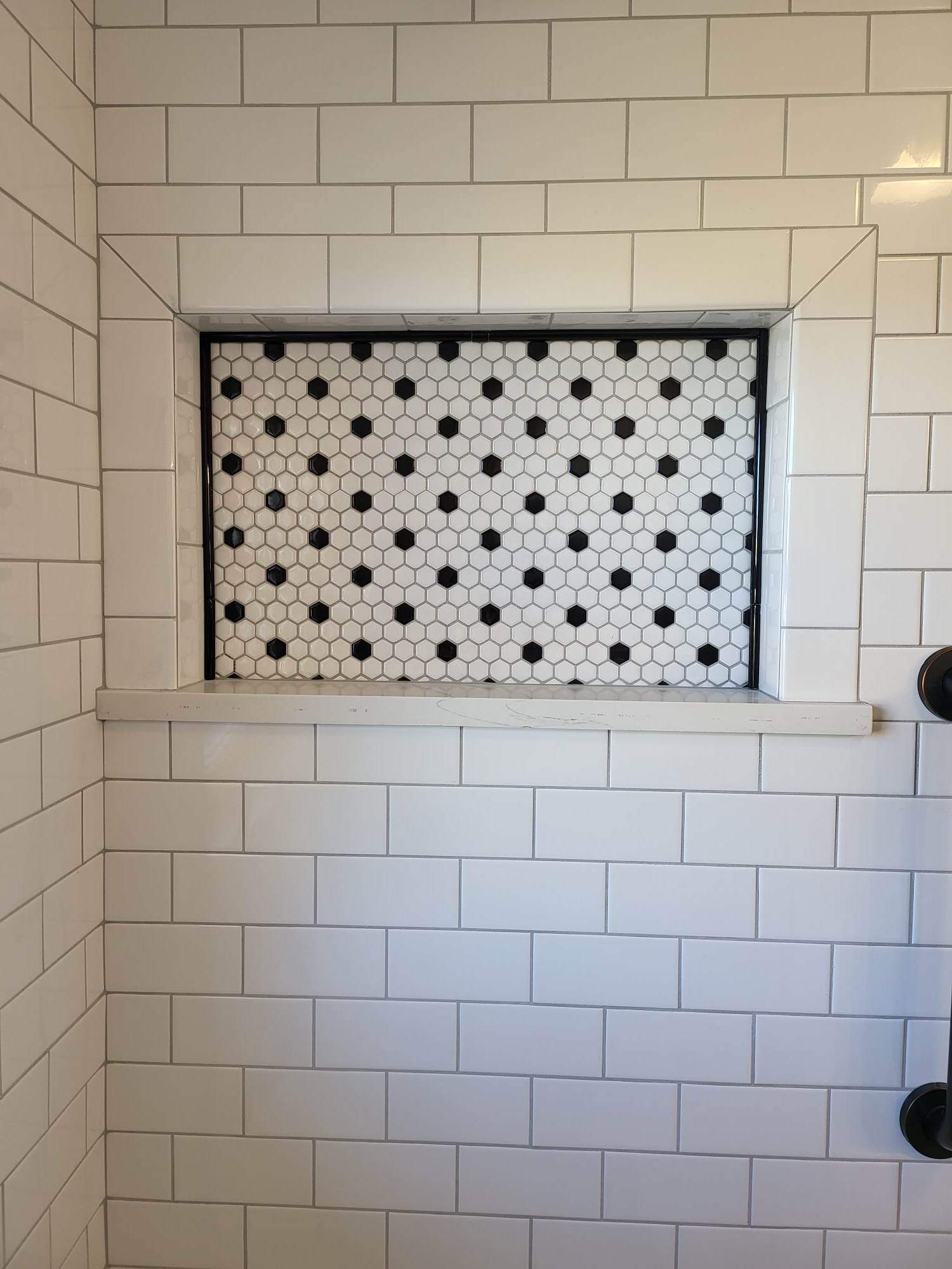 A shower stall with white tiles and black polka dots