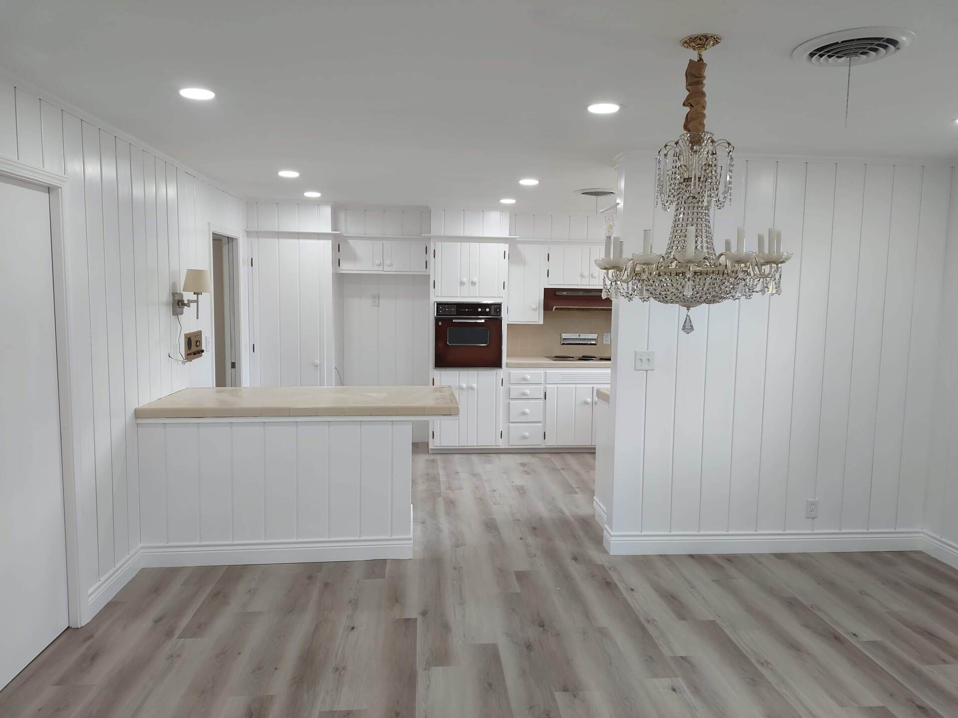 An empty kitchen with white cabinets and a chandelier hanging from the ceiling.