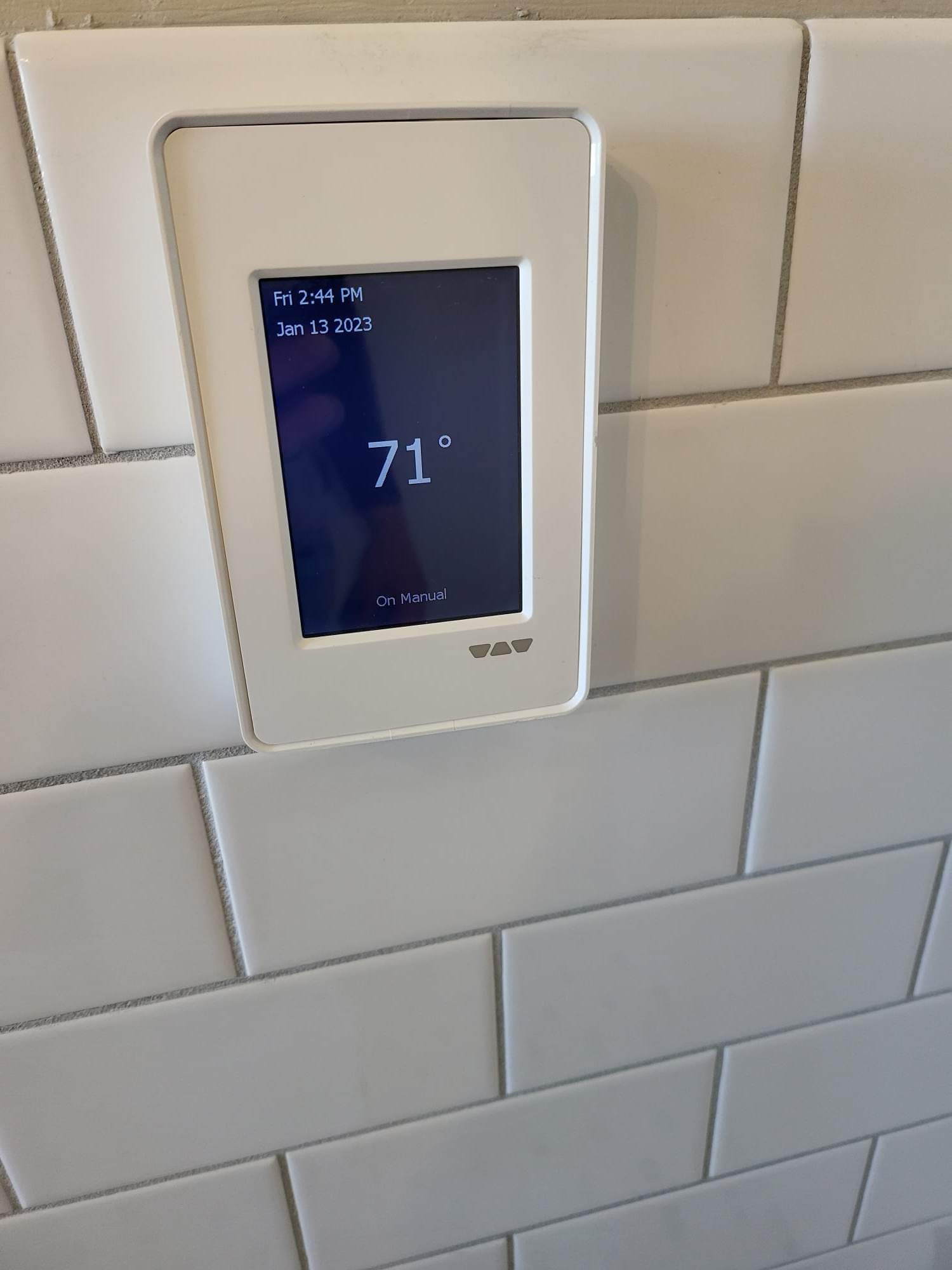 A white thermostat is hanging on a white tiled wall.