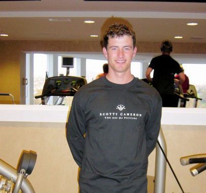 A man wearing a scott cameron shirt stands in a gym