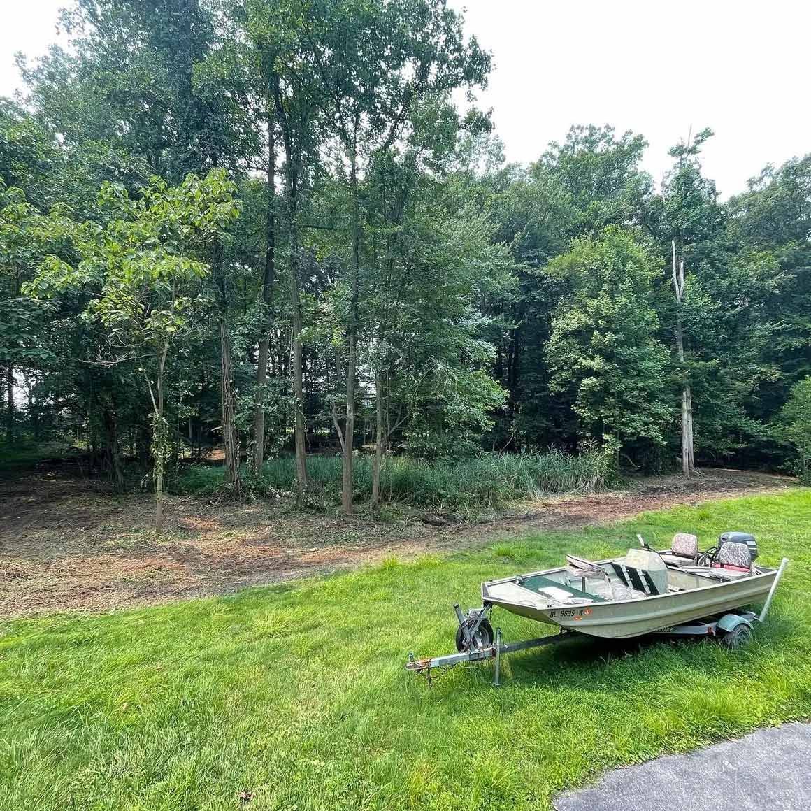 A small boat on a trailer sits on a grassy area, trees in the background.