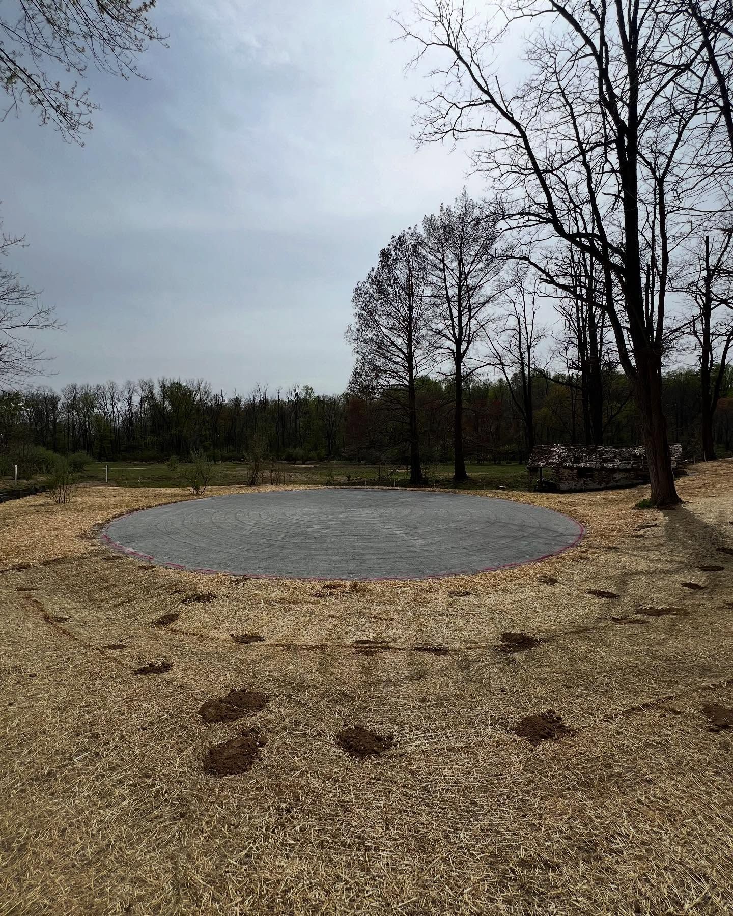 Circular paved area surrounded by wood chips, trees in the background, cloudy sky.