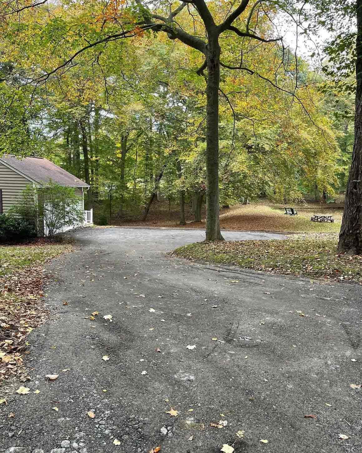Asphalt driveway leads to a small building surrounded by trees with autumn foliage.
