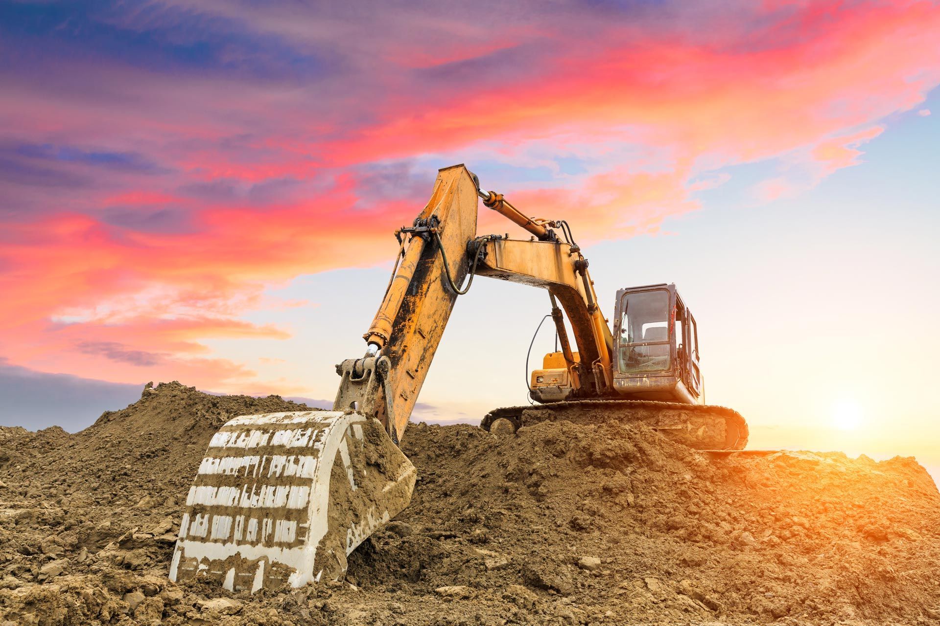 Excavator digging at a construction site under a vivid sunset sky