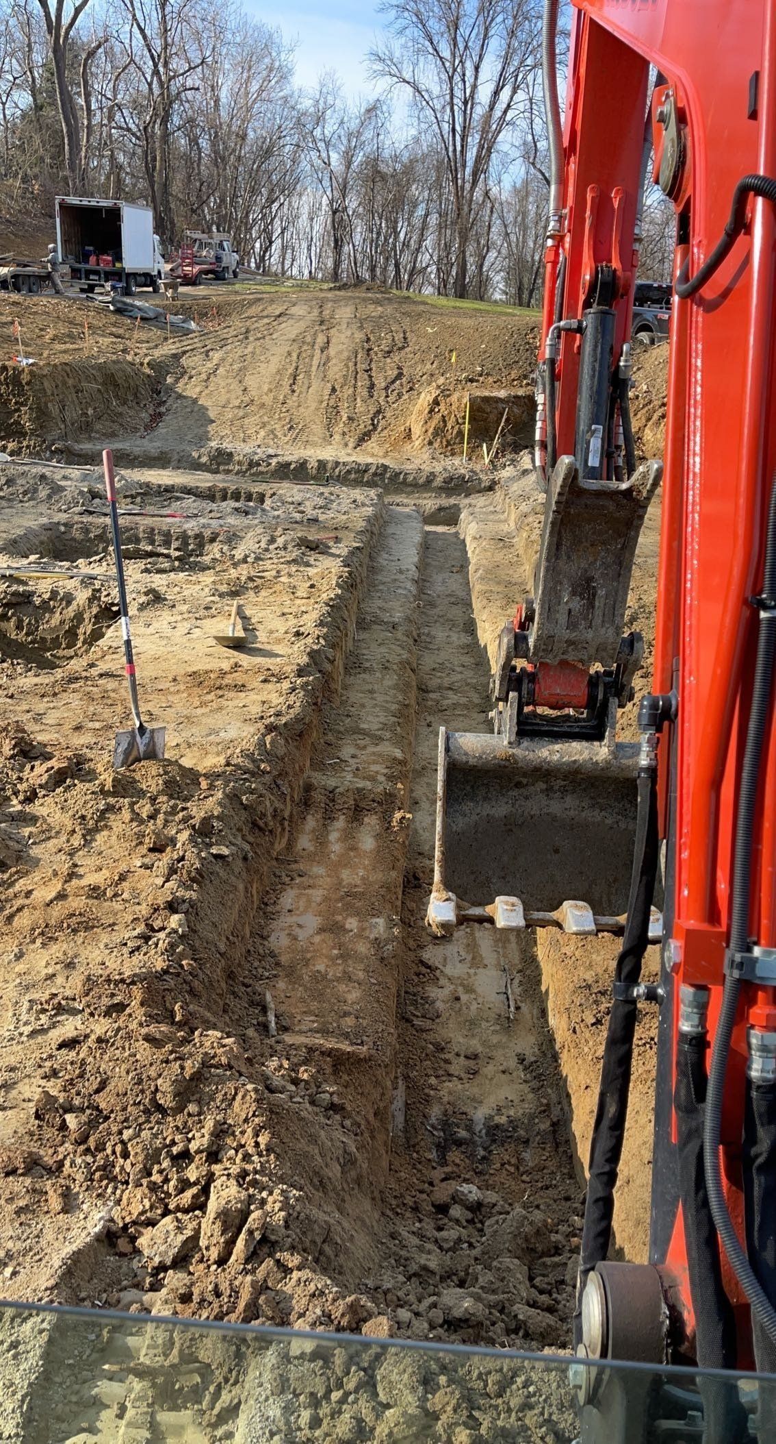 An orange excavator digging a long trench in brown earth at a construction site.