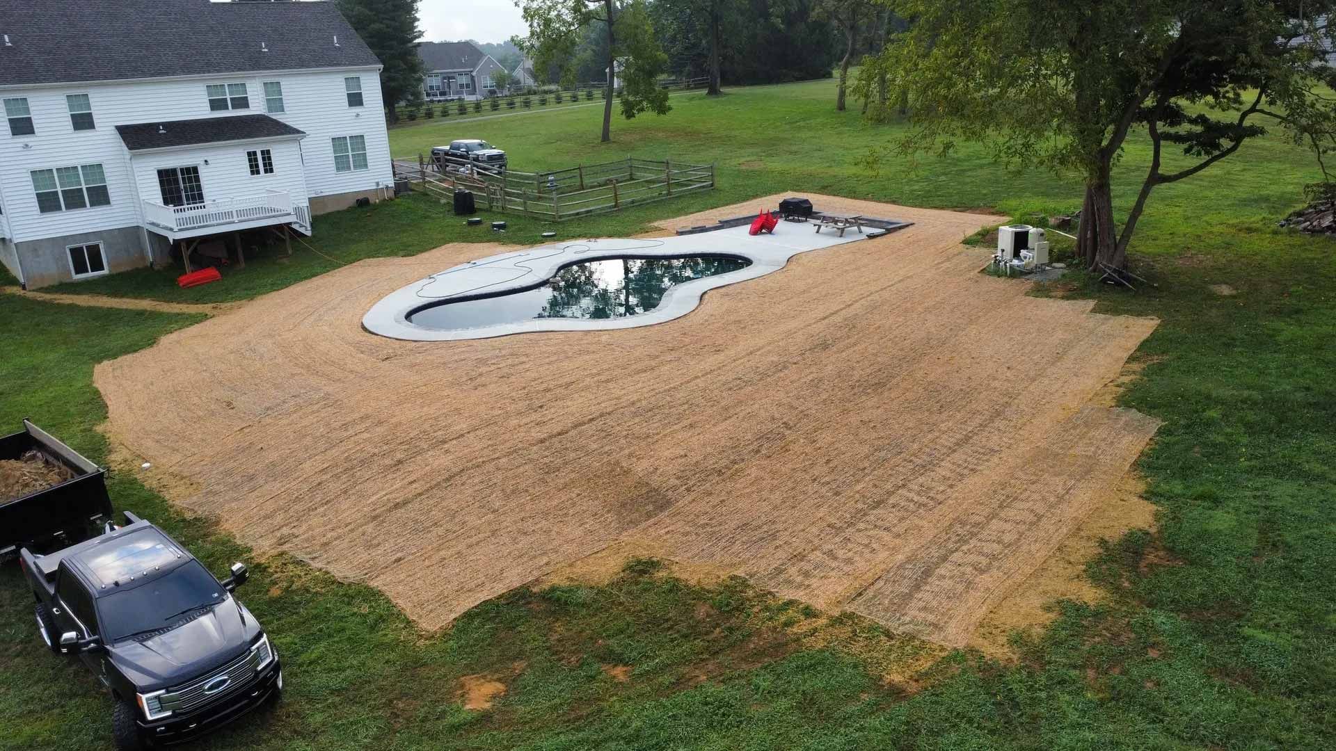 Aerial view of a swimming pool construction site. A house sits in the background, a truck is parked in the foreground.
