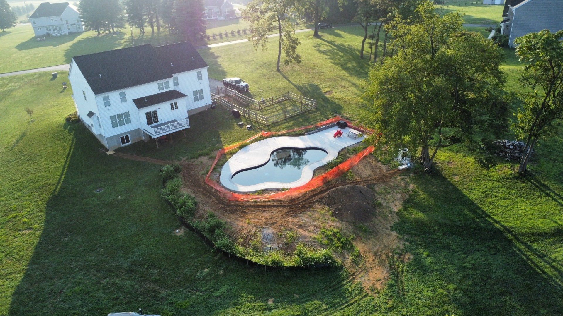 Aerial view of a home with a skatepark under construction in the backyard, surrounded by orange safety fencing and grassy yard.