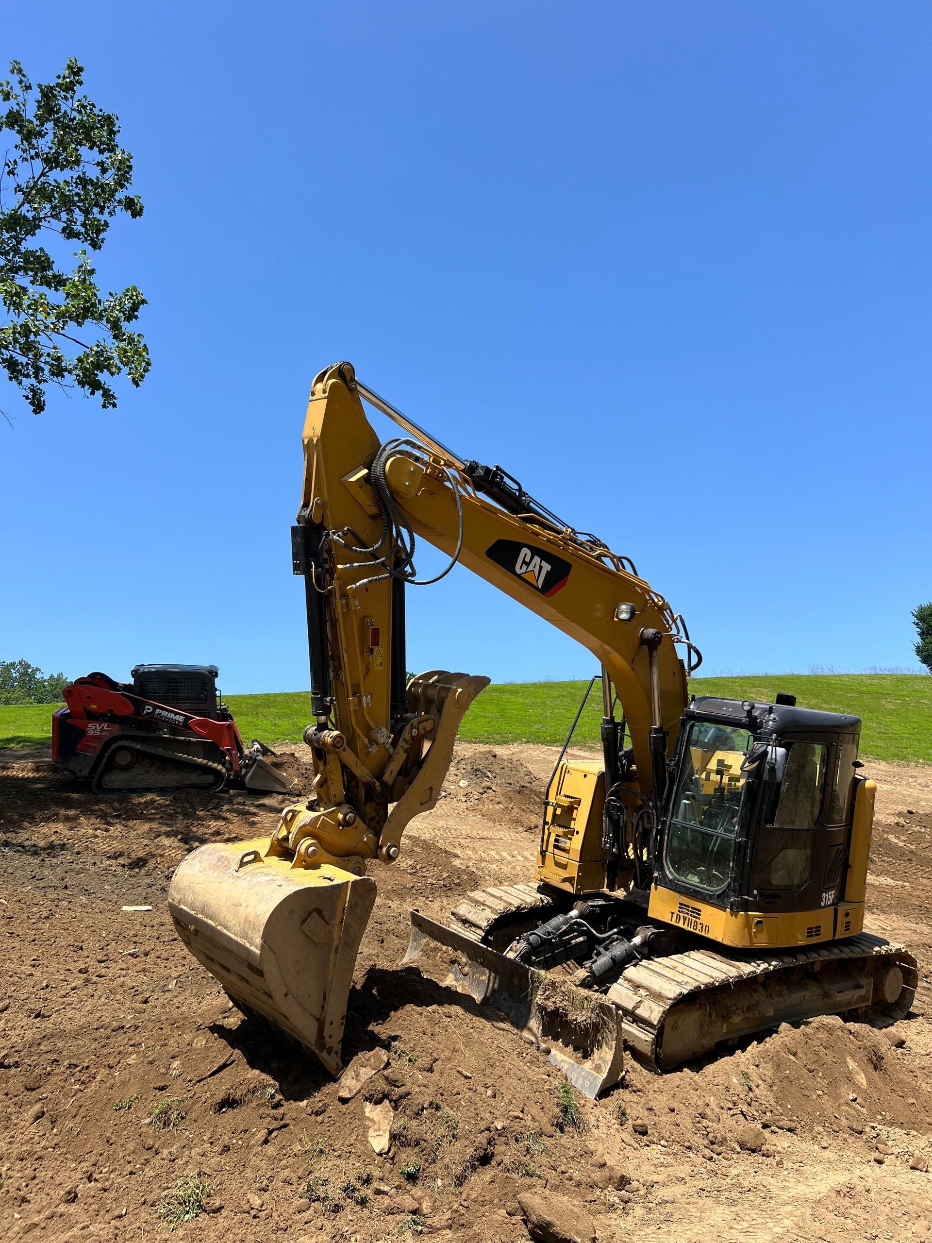 Yellow Caterpillar excavator on dirt, sunny day. A small red skid steer is in the background.