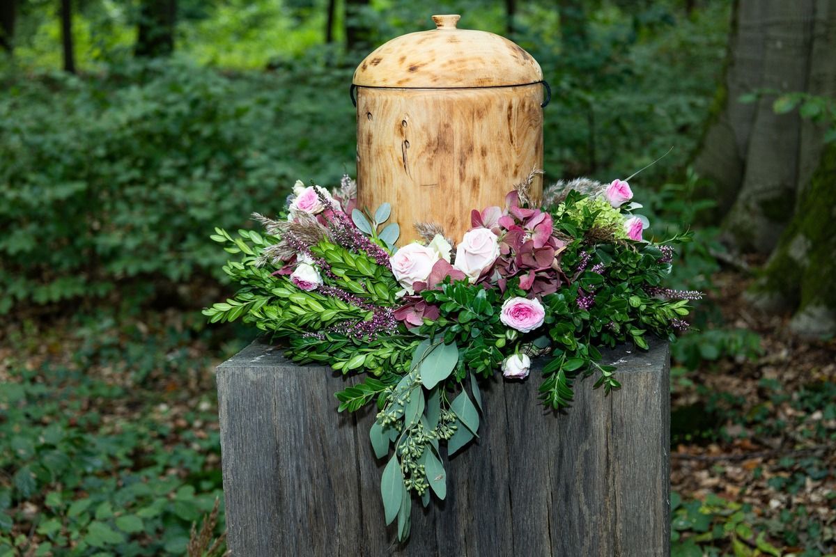 Wooden urn with floral arrangement on a tree stump in a forest.