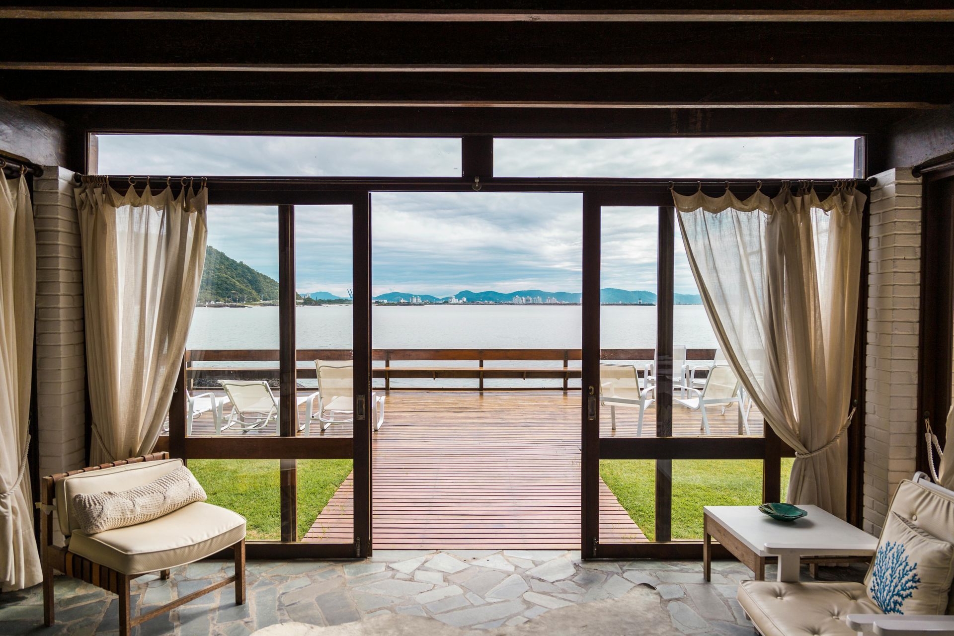 Interior with wooden door to a deck overlooking a body of water with mountains.