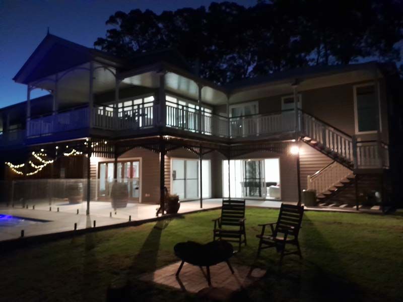 A large house is lit up at night with a fire pit in front of it