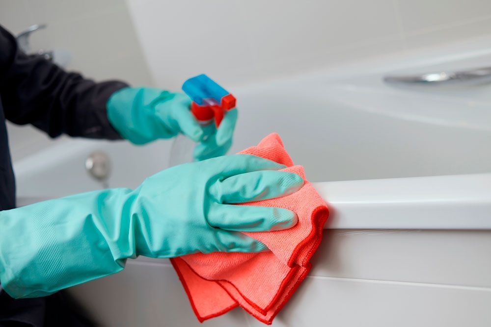A person wearing gloves is cleaning a bathtub with a towel and spray bottle.