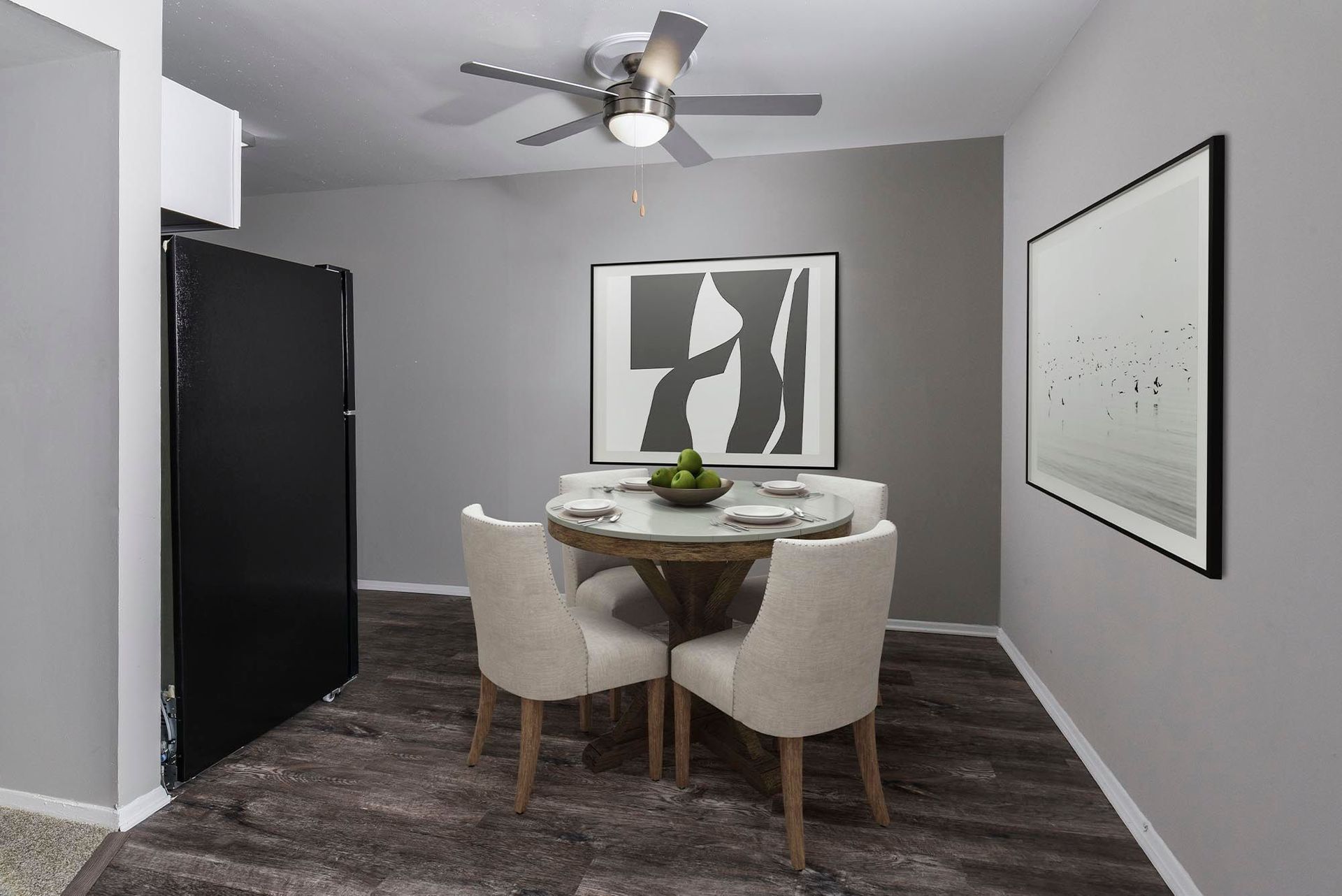 Dining area with a round table, four chairs, art, and a ceiling fan.