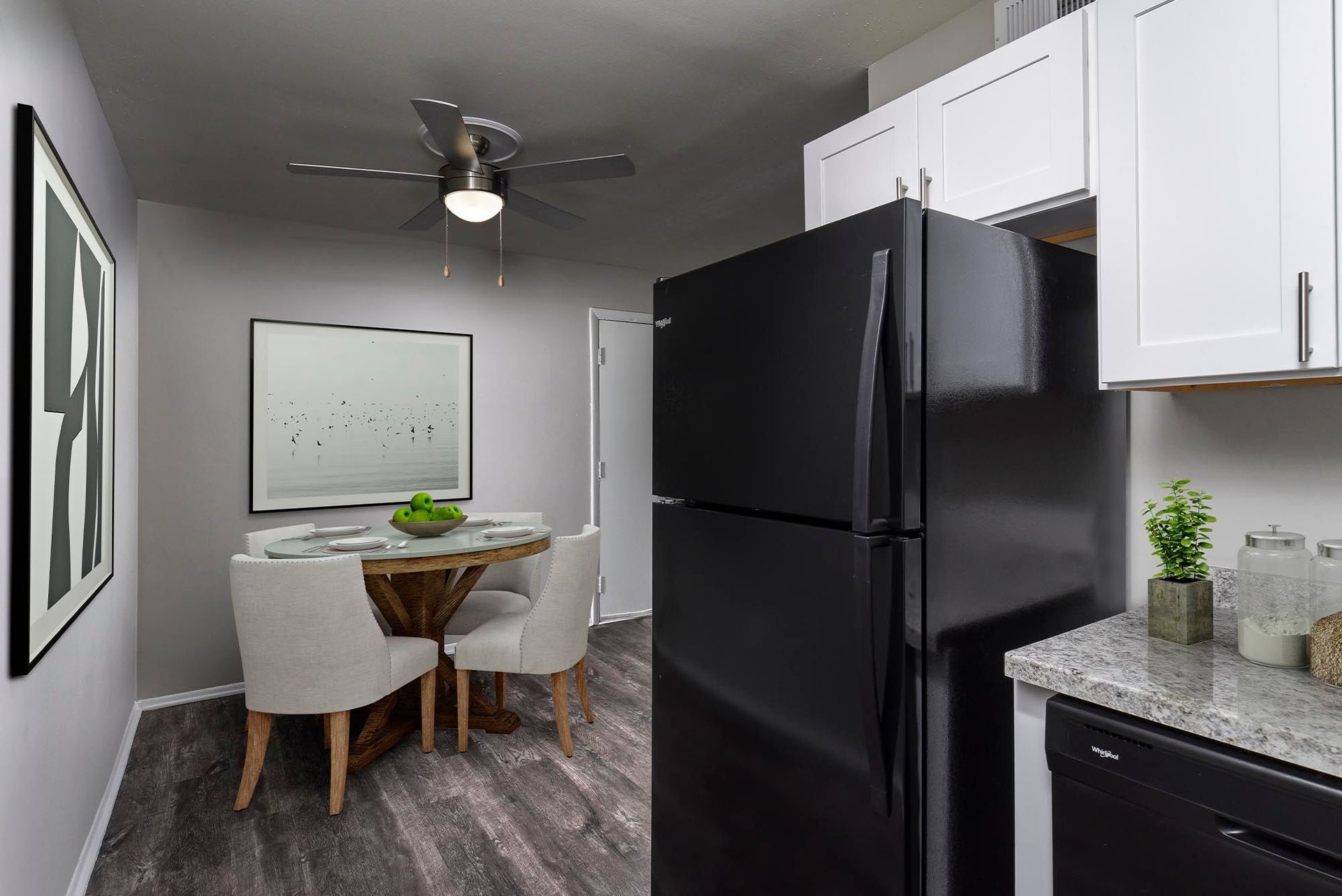 Kitchen and dining area with black refrigerator, wooden table, and white cabinets.