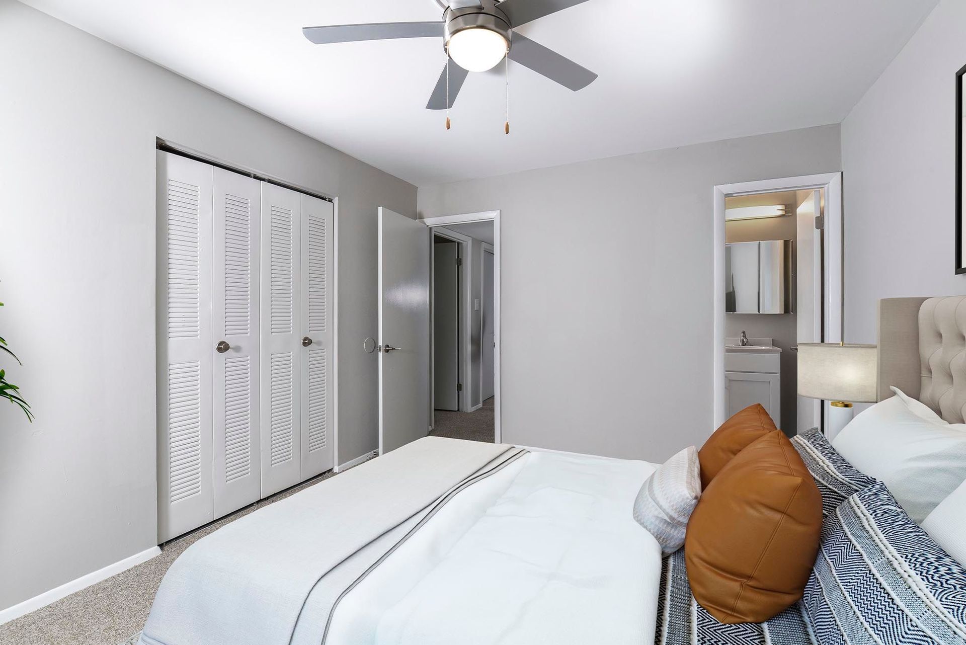 Bedroom with bed, closet, and doorway to bathroom. Gray walls, white trim, ceiling fan.