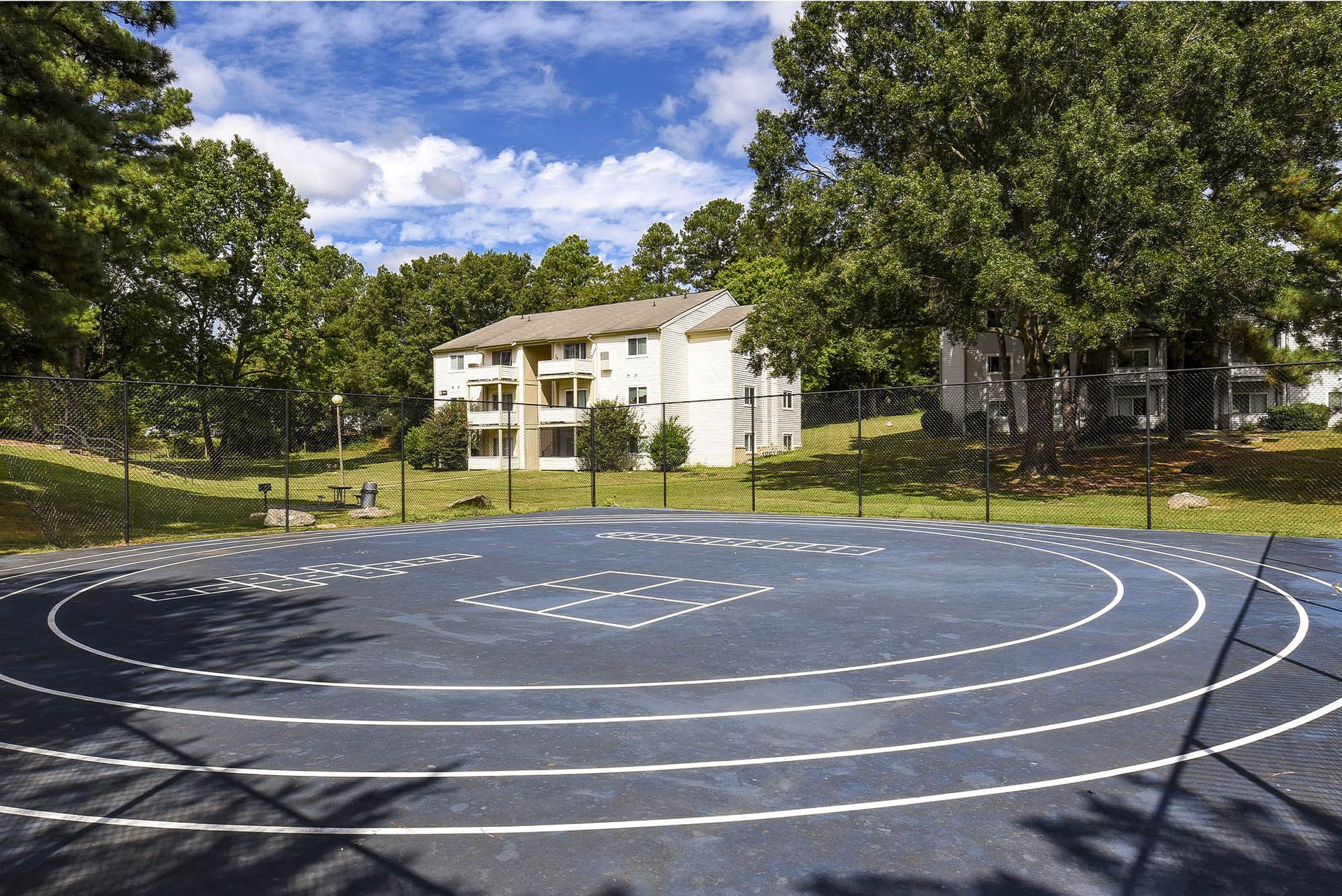 Blue running track with white lines, surrounded by trees and a white building under a blue sky.