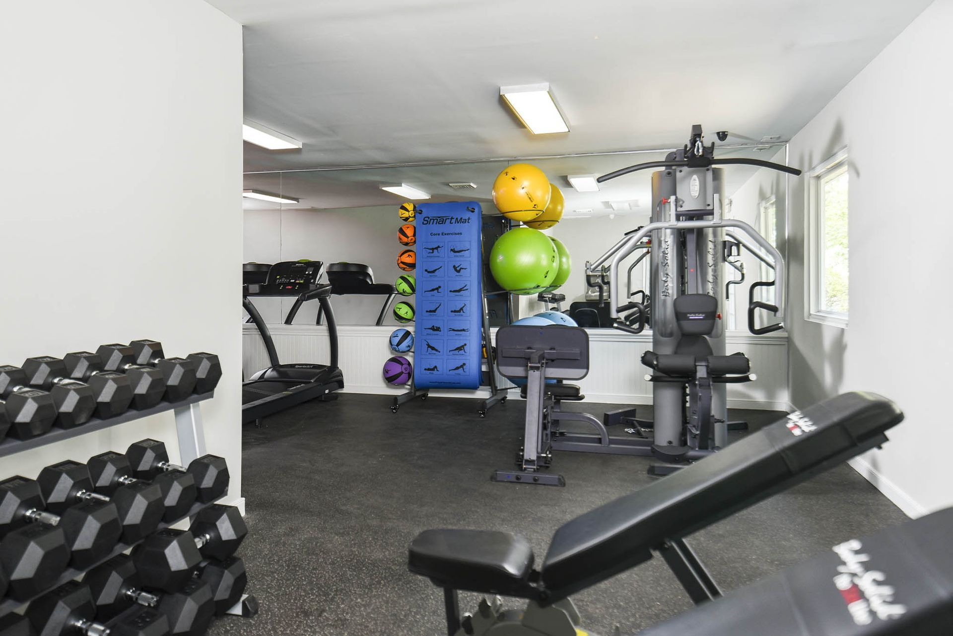 Gym with weights, treadmill, exercise equipment, and mirrors; black flooring and white walls.