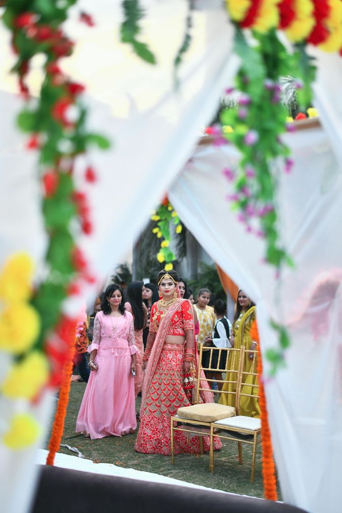 Two women in pink and red dresses at an outdoor floral wedding entrance