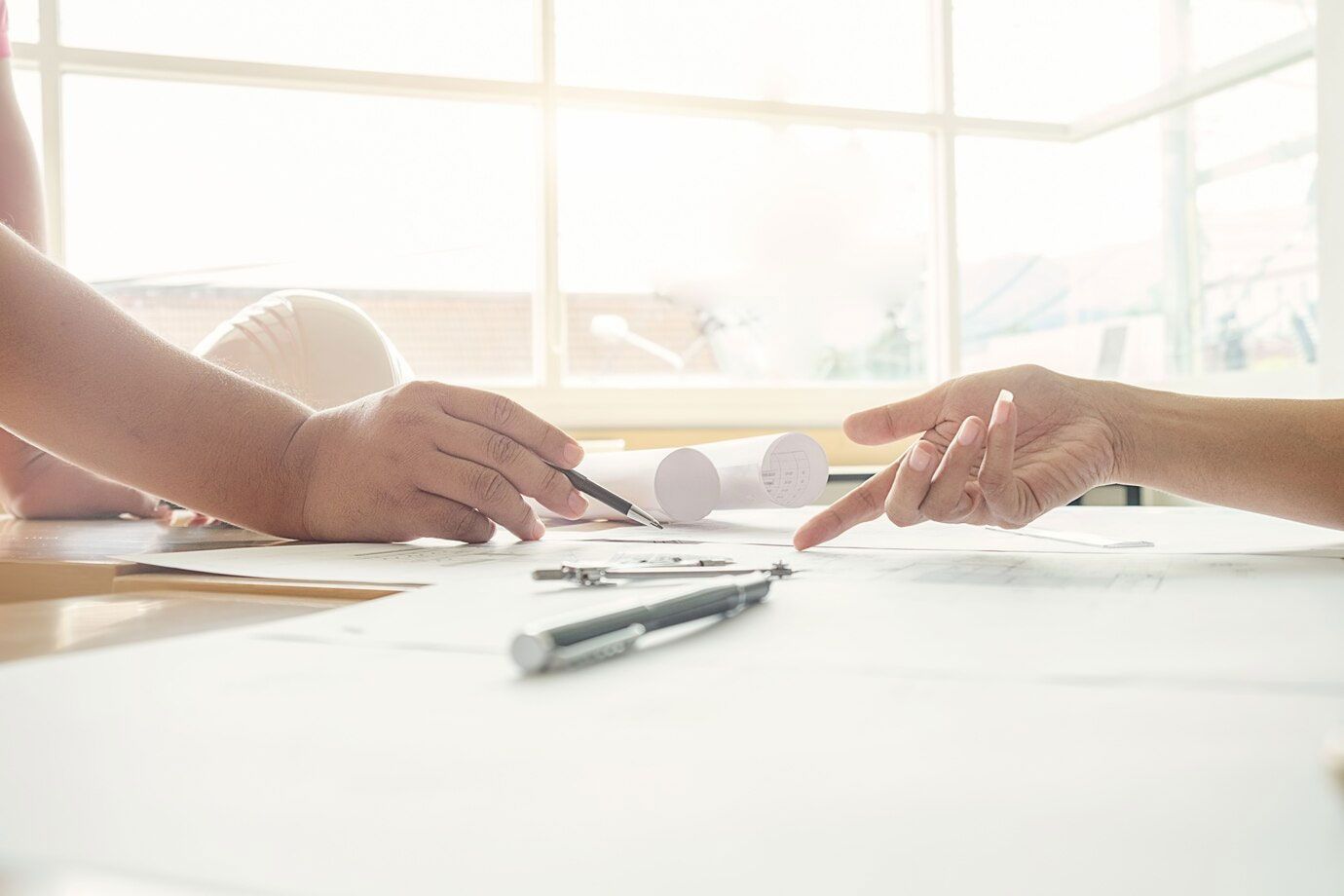 two people are sitting at a table pointing at a piece of paper .
