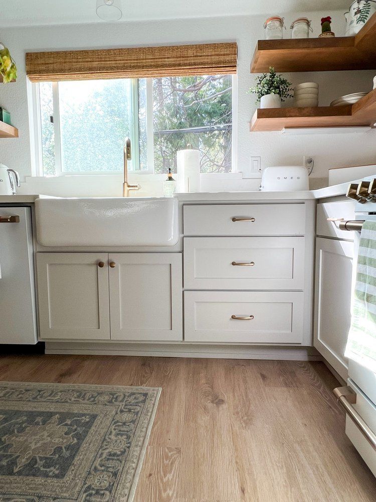 a kitchen with white cabinets , a sink , a stove , and a rug .
