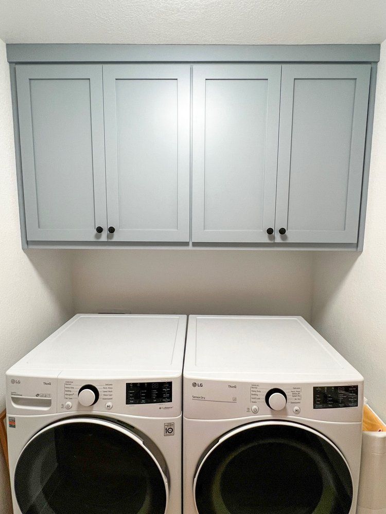 a washer and dryer are in a laundry room under cabinets .