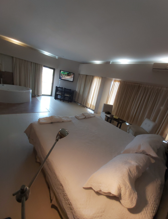 Una habitación de hotel amplia y luminosa con una cama grande, una bañera redonda y cortinas que van del suelo al techo.